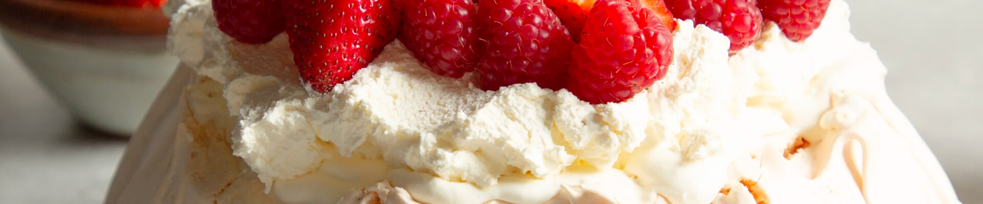 Fresh raspberries and strawberries sit atop a home made pavlova topped with whipped cream.